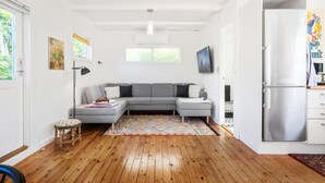 Un salon moderne avec un canapé d’angle gris, un plancher en bois, un petit tabouret et un réfrigérateur.