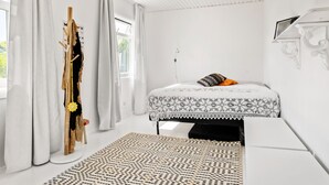 Une chambre à coucher comprenant un lit, une table de chevet, une fenêtre avec des rideaux et un luminaire fixé au mur.
