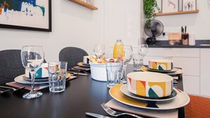 Une table à manger dressée avec des assiettes, des verres et des couverts, ainsi qu’un panier de fruits et une bouteille de jus d’orange.