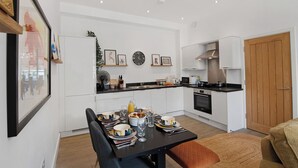 Une cuisine moderne avec des meubles blancs, une table à manger pour quatre personnes et une porte en bois.