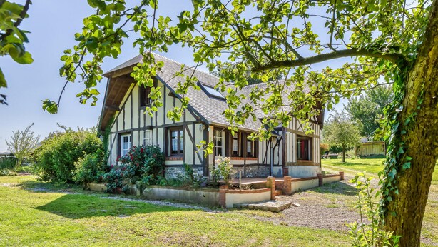 A traditional half-timbered house with a sloped roof, surrounded by a well-maintained garden and a gravel pathway.