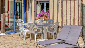 An outdoor seating area with a table and four chairs, a sun lounger, and a potted plant with pink flowers.