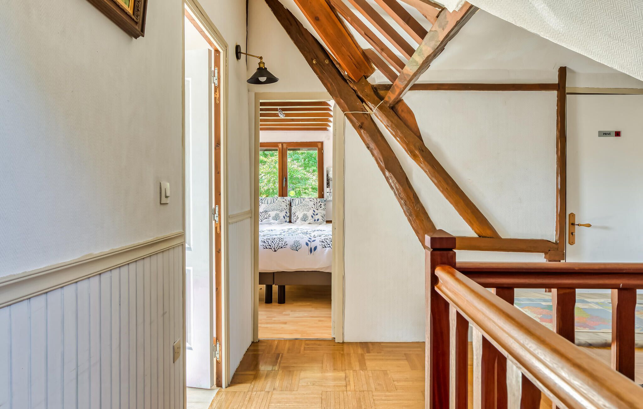 Een houten trap die leidt naar een slaapkamer met een bed en een raam.
