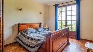 Ein Schlafzimmer mit einem hölzernen Bett, einem Nachttisch mit Lampe und einem Fenster mit blauen Vorhängen.