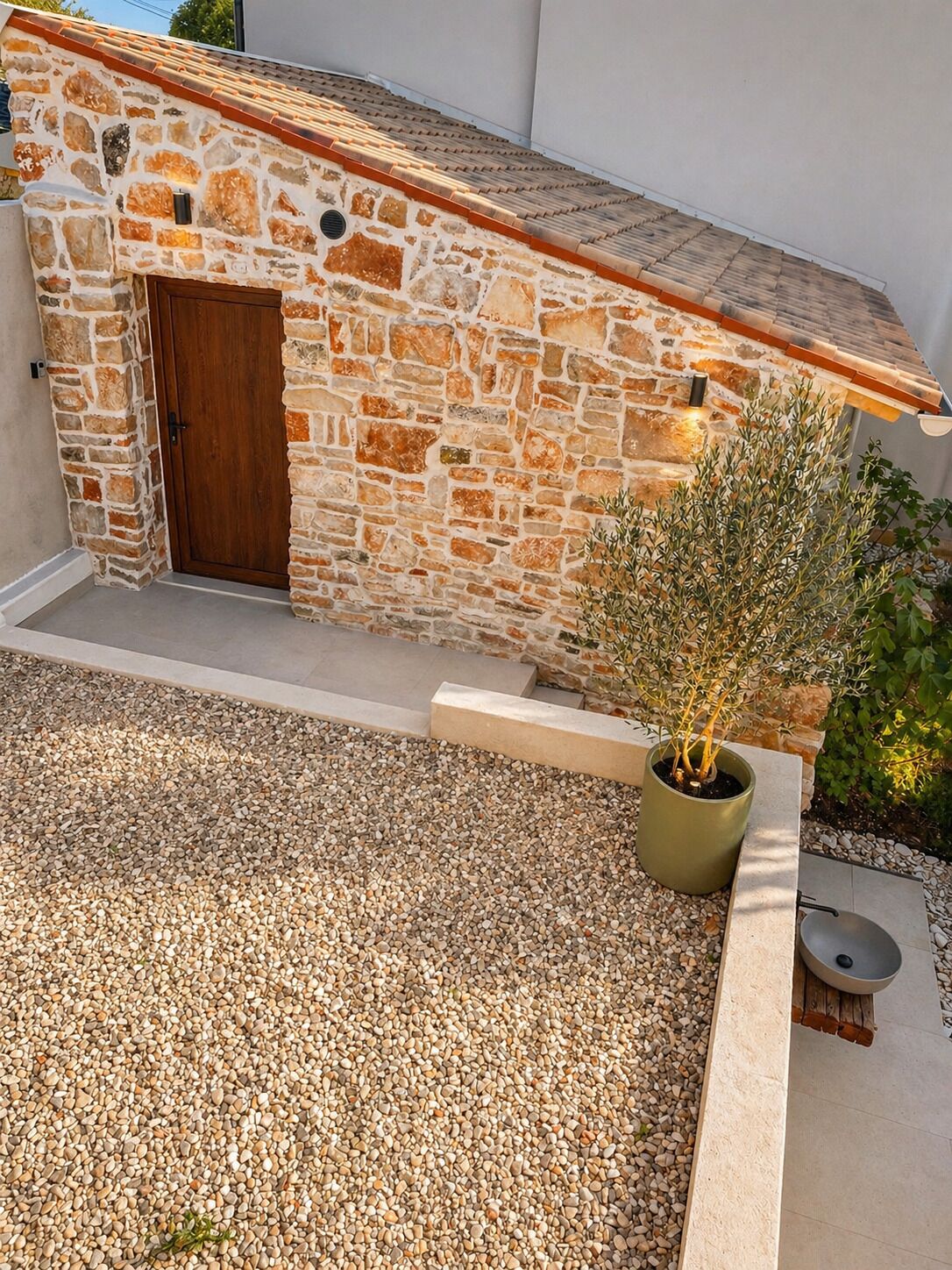 A stone building with a wooden door, a gravel courtyard, and a potted plant.