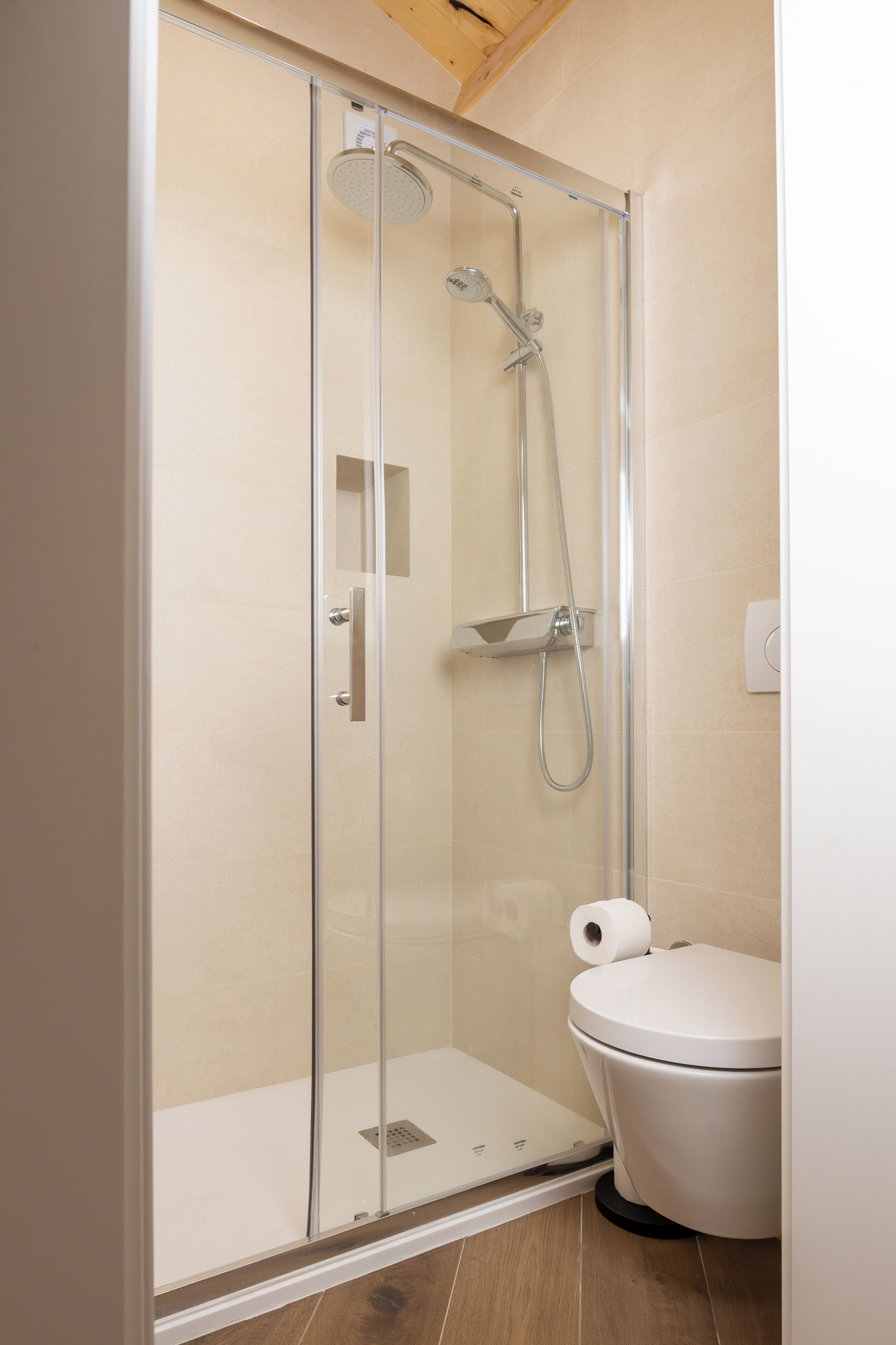 A modern bathroom with a glass-enclosed shower, a white toilet, and a wooden ceiling.