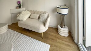 Ein modernes Wohnzimmer mit einem beigefarbenen Sofa, weichen weißen Kissen, einem weißen Teppich und einer Stehlampe.