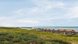 Eine Küstenlandschaft mit einer Reihe von Holzstrandhäusern und einem großen Gebäude im Hintergrund.