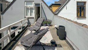 Ein Balkon mit zwei Liegestühlen, einem kleinen Topfpflanzen und einem Mülleimer.