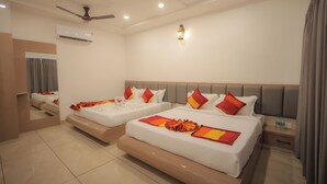 Een hotelkamer met twee bedden, een plafondventilator, een airconditioningapparaat, een nachtkastje met een lamp en een spiegel.