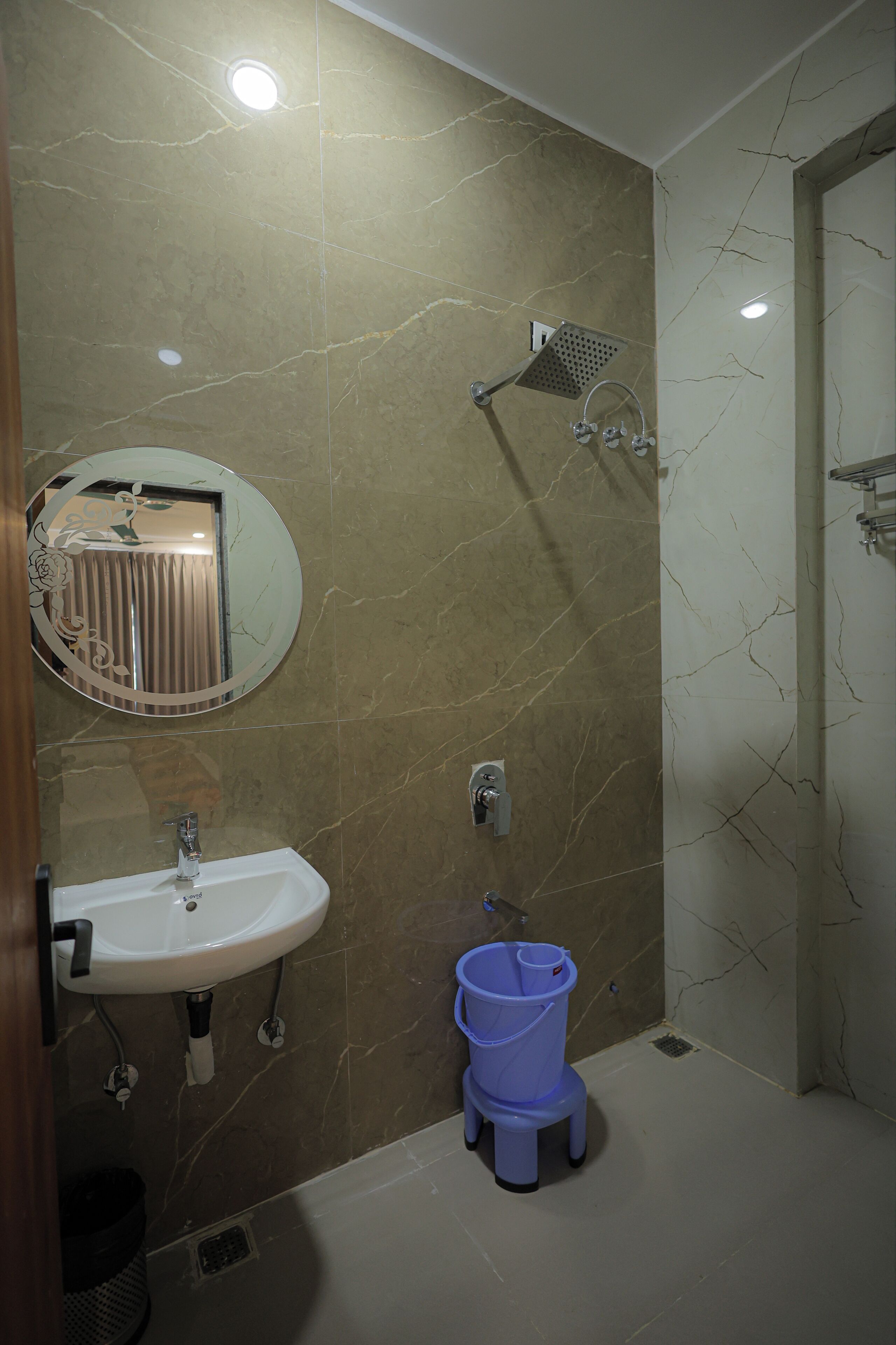 A bathroom with a sink, mirror, shower, and a blue bucket.
