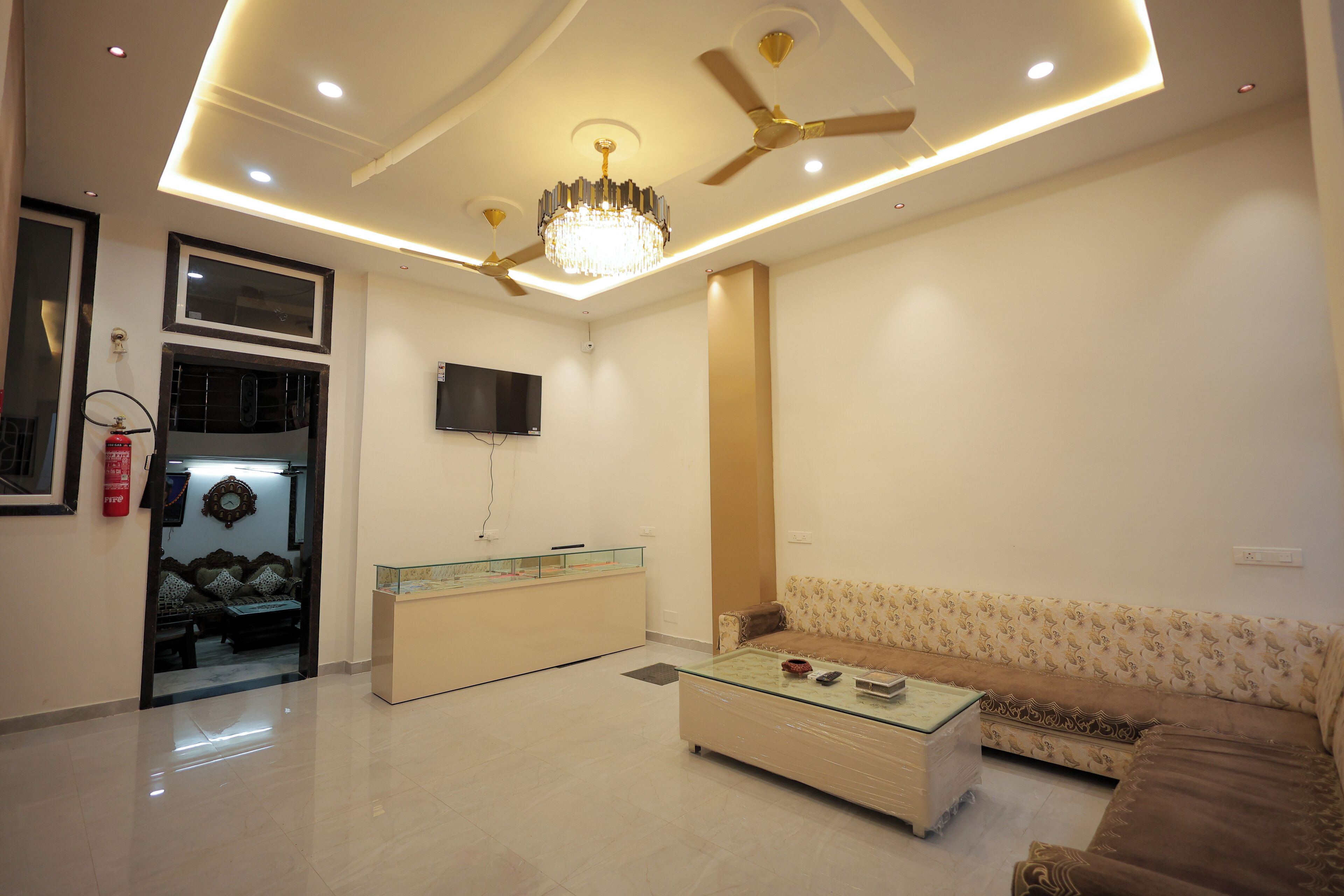 A modern living room with a sofa, coffee table, ceiling fan, chandelier, and a television mounted on the wall.