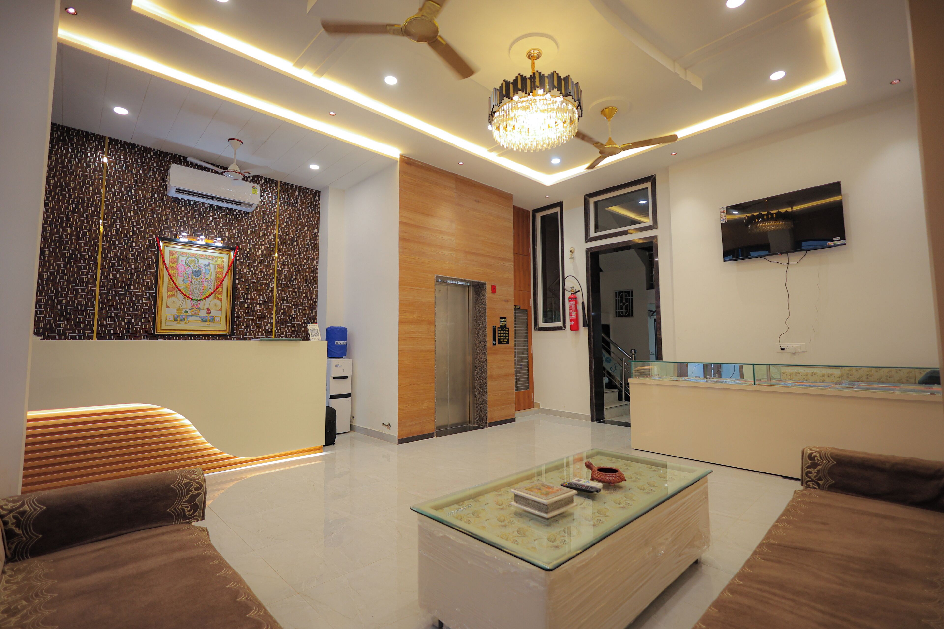A modern hotel lobby with a reception desk, seating area, and a chandelier.
