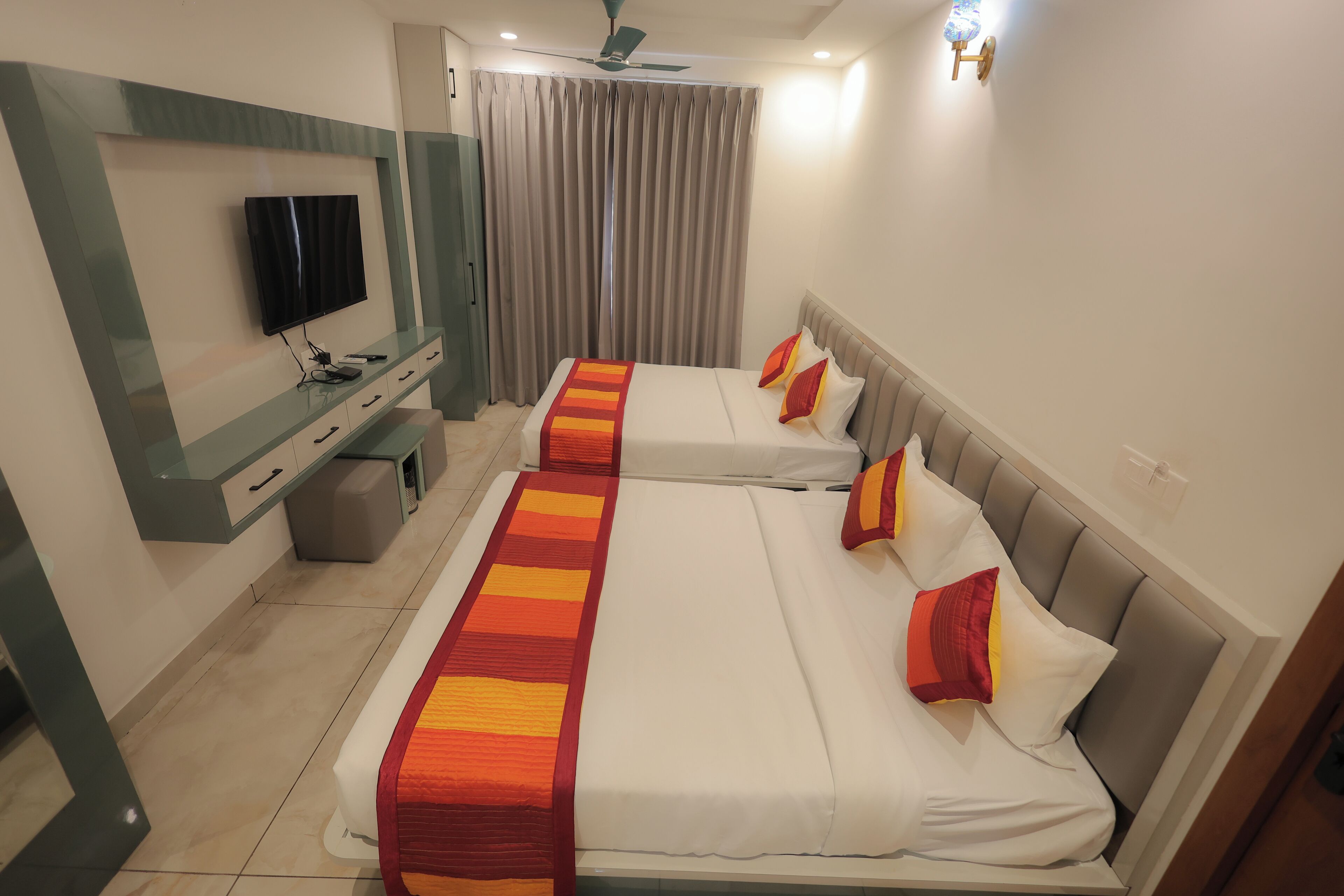 A hotel room with two beds, a TV, a ceiling fan, and a window with curtains.
