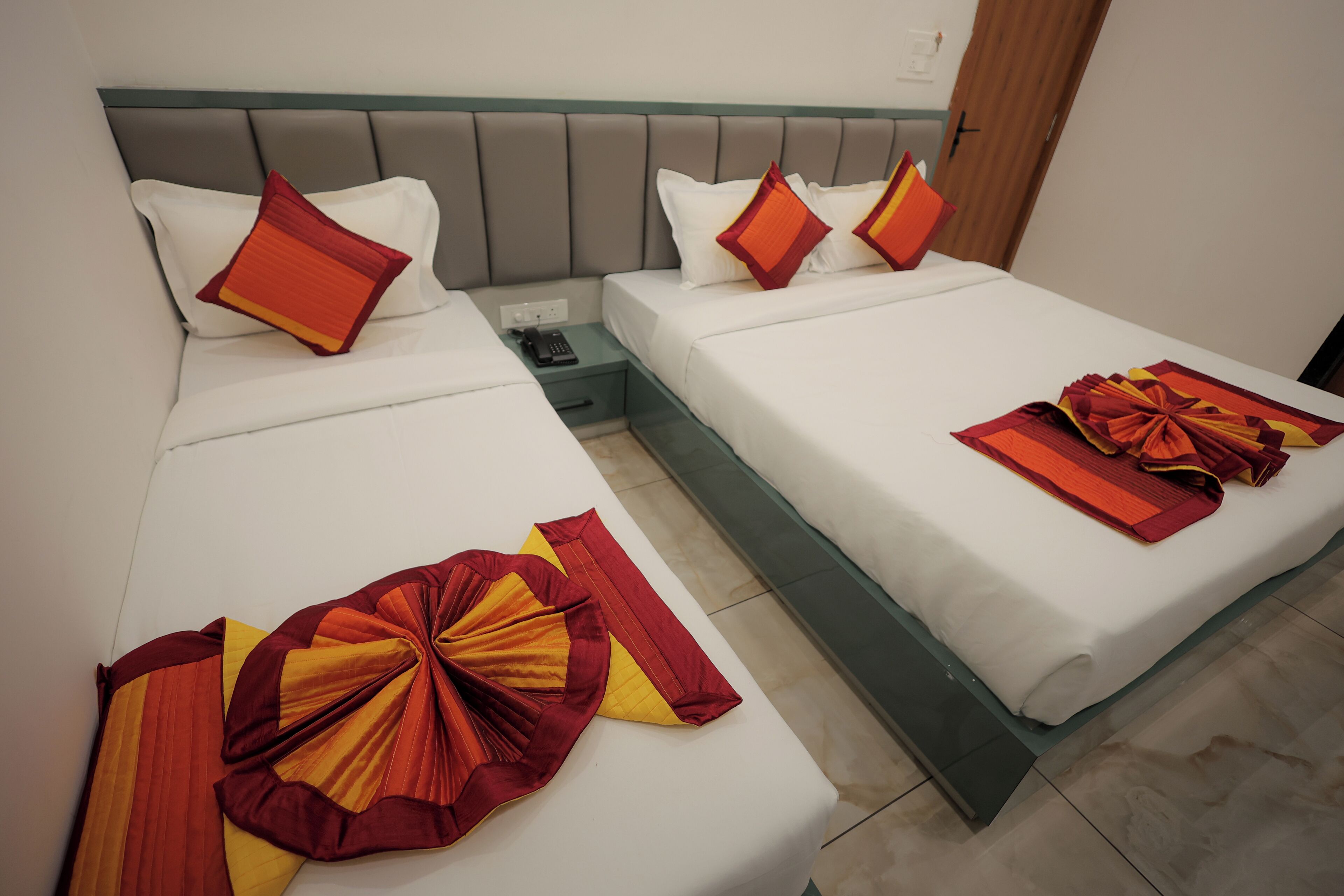 A hotel room with two beds, each with white bedding and red-orange decorative pillows.