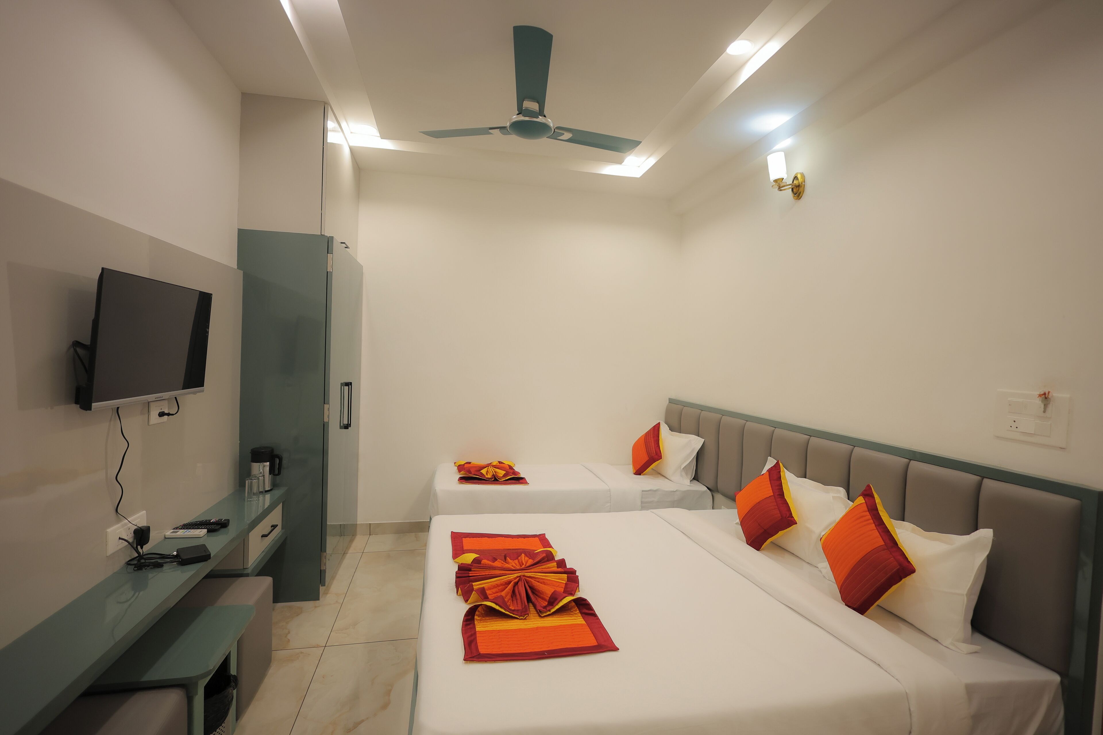A hotel room with two beds, a TV, a desk, and a ceiling fan.