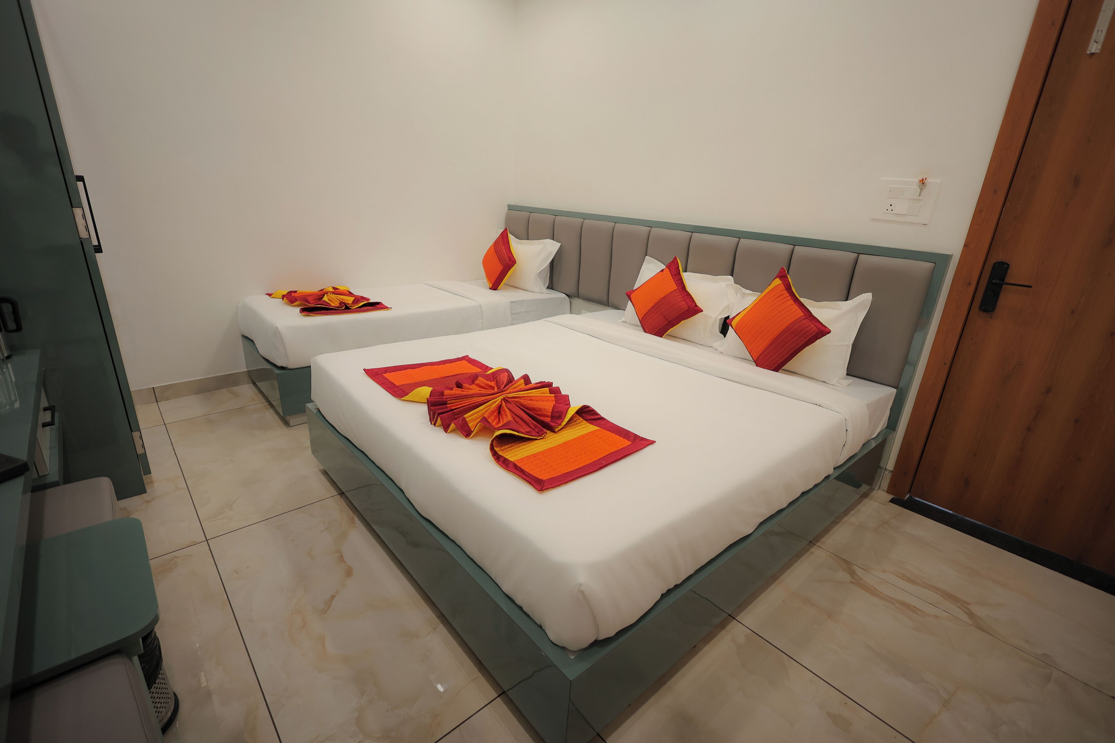 Een hotelkamer met twee bedden, elk voorzien van witte lakens en oranje sierkussens.