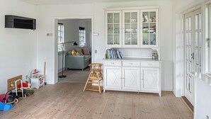 Een ruime kamer met een houten vloer, een witte kast met glazen deuren, een bank en een kleine houten stoel.