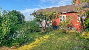 Een rode woning met een witte veranda en een tuin ervoor.