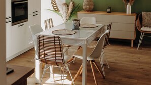 Un espace repas moderne avec une table blanche, des chaises en osier et un luminaire suspendu.
