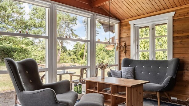 Una habitación acogedora con detalles de madera, ventanas amplias y una mesa de madera con sillas.