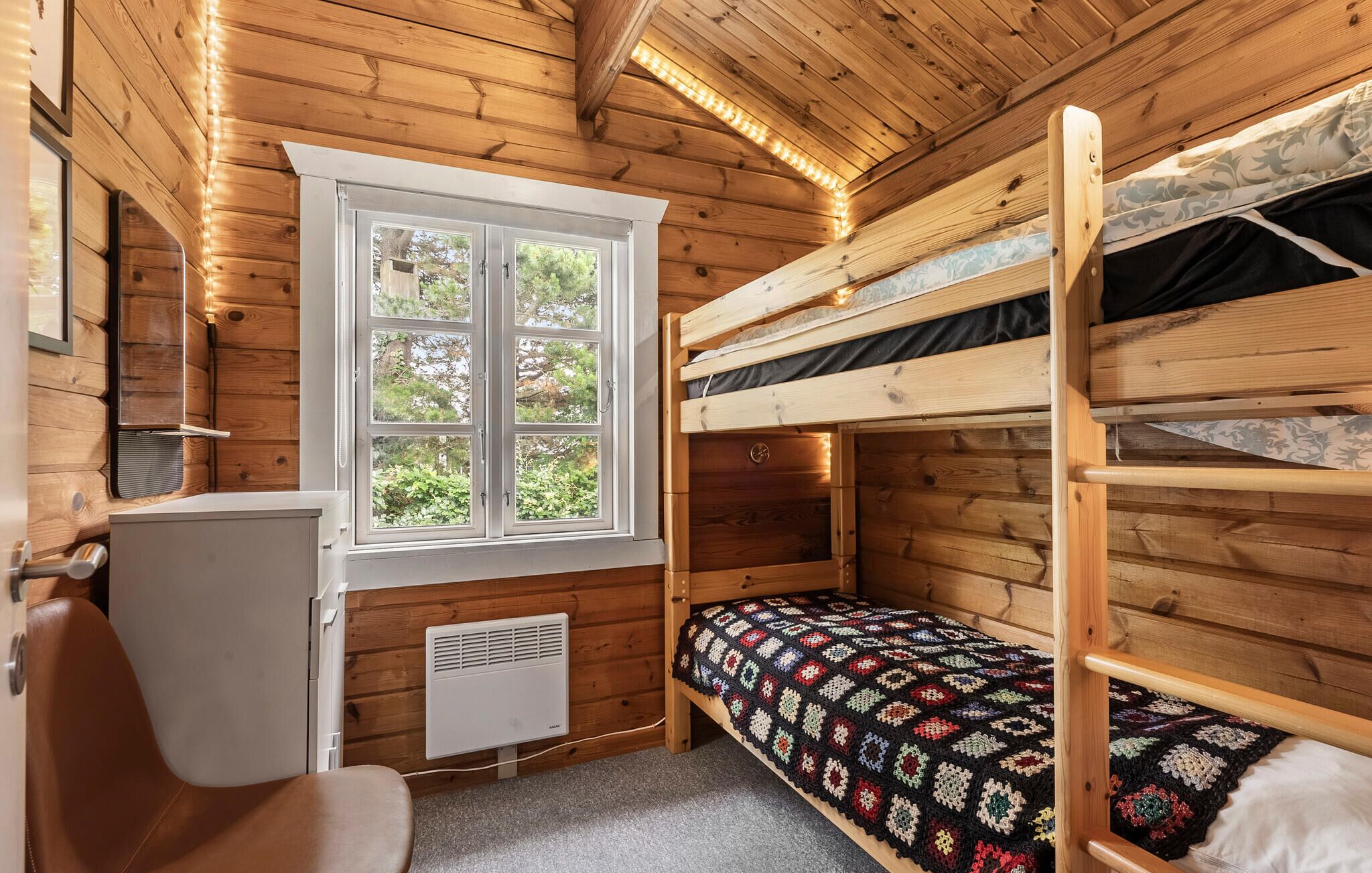 A compact wooden cabin room with bunk beds, a window, a desk, and a radiator.