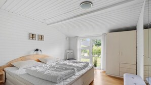 Ein Schlafzimmer mit Holzboden, einem Bett mit weißer Bettwäsche, einem Nachttisch, einem Sessel und einem Kleiderschrank.