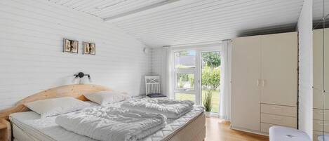 A bedroom with a wooden ceiling, a bed with white bedding, a bedside table, a chair, and a wardrobe.