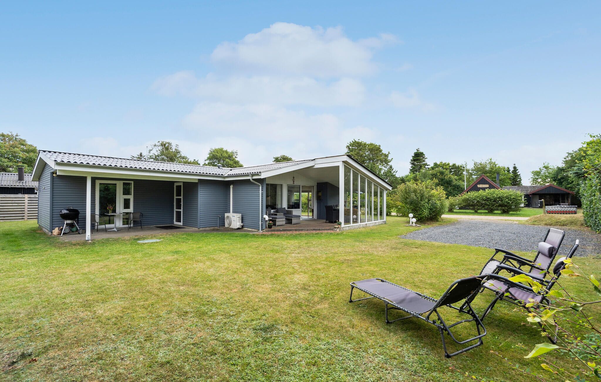 Ein Bungalow mit überdachter Terrasse, Grill und Rasen mit Gartenmöbeln.