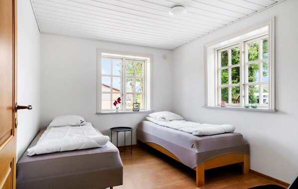 A bedroom with two single beds, a small round table, and two windows with views of greenery.