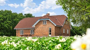 Ein Haus aus Ziegeln mit einem roten Ziegeldach, einem Schornstein und einer hölzernen Bank davor.
