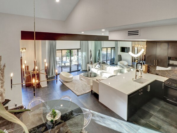 Una cocina moderna con una isla central, un comedor con mesa de vidrio y una sala de estar con sofá y sillones.
