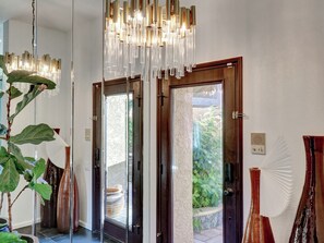 A modern interior with a glass door leading to an outdoor area, a large plant, and a unique chandelier. - The Fox's Den at Ironwood Country Club (Palm Desert)