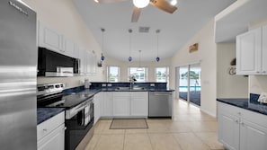 A modern kitchen with white cabinets, stainless steel appliances, and a large island. - Casa de La Vista Pool Spa With Lakefront View (Cape Coral)