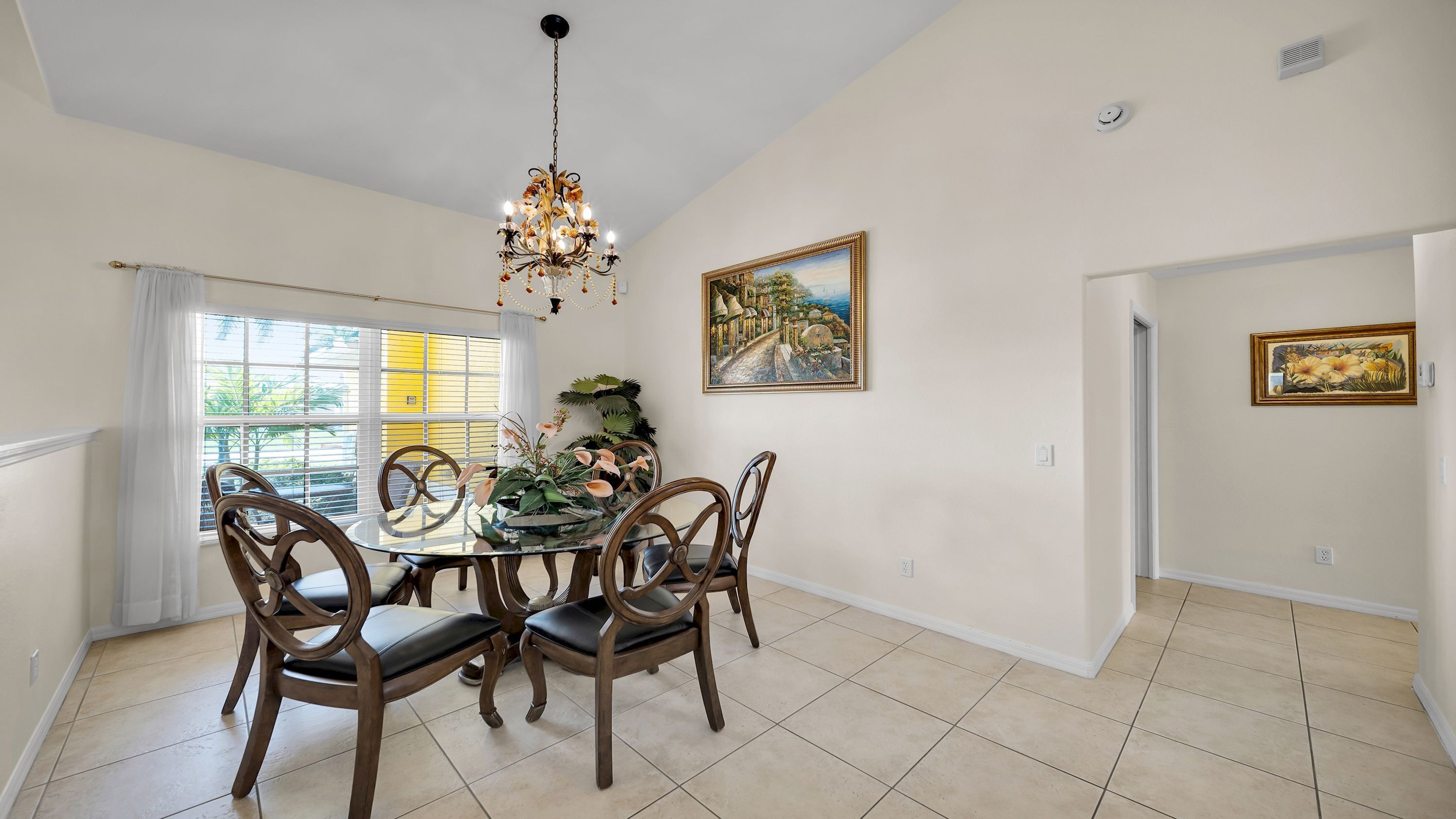 A dining room with a chandelier, a table with chairs, and two framed paintings on the walls.