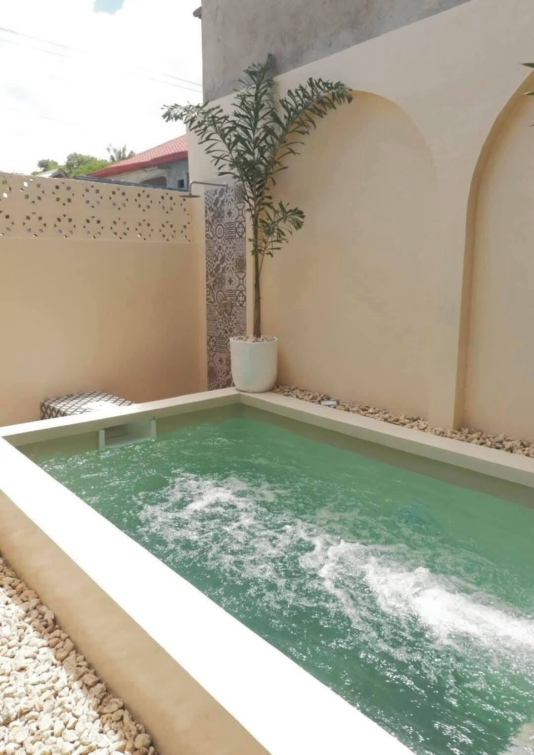 Une piscine rectangulaire bordée de blanc, entourée de murs de couleur beige et agrémentée d’une section de mur à motifs.