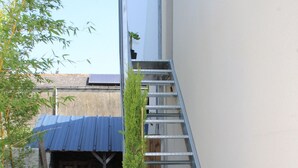 A narrow outdoor corridor with a metal staircase, a potted plant, and a bicycle.