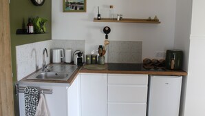A kitchen with a sink, a coffee maker, a kettle, and a refrigerator.