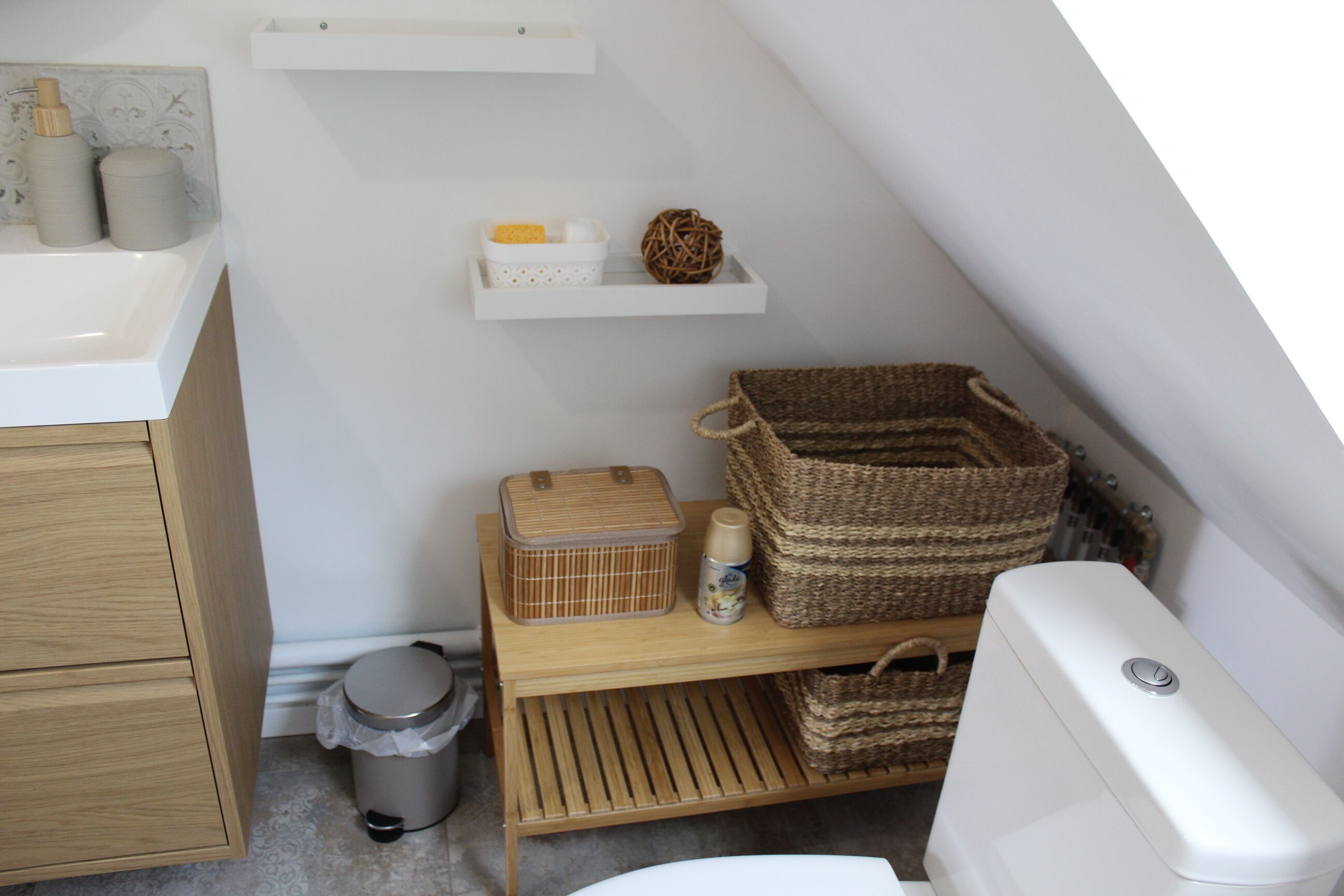 A small bathroom with a wooden cabinet, a toilet, and a shelf with baskets and toiletries.