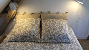 A bedroom with a wooden ceiling, two patterned pillows, and a wall-mounted lamp.