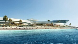 Um hotel moderno à beira-mar, com área de praia, palmeiras e um veleiro.
