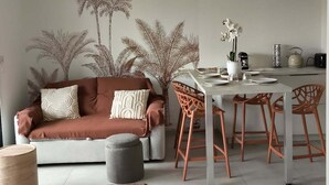 Uma sala de estar moderna com um sofá marrom, uma mesa de jantar com quatro cadeiras e uma grande planta em vaso.