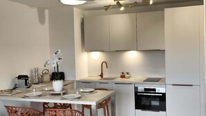Uma cozinha moderna com armários brancos, uma ilha central com assentos e uma luminária pendente.