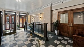 A lobby with a checkered floor, wooden doors, and a staircase with a railing.