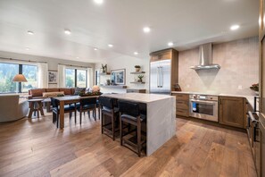 A modern kitchen with a central island, wooden flooring, and a large window offering a view of the outdoors.