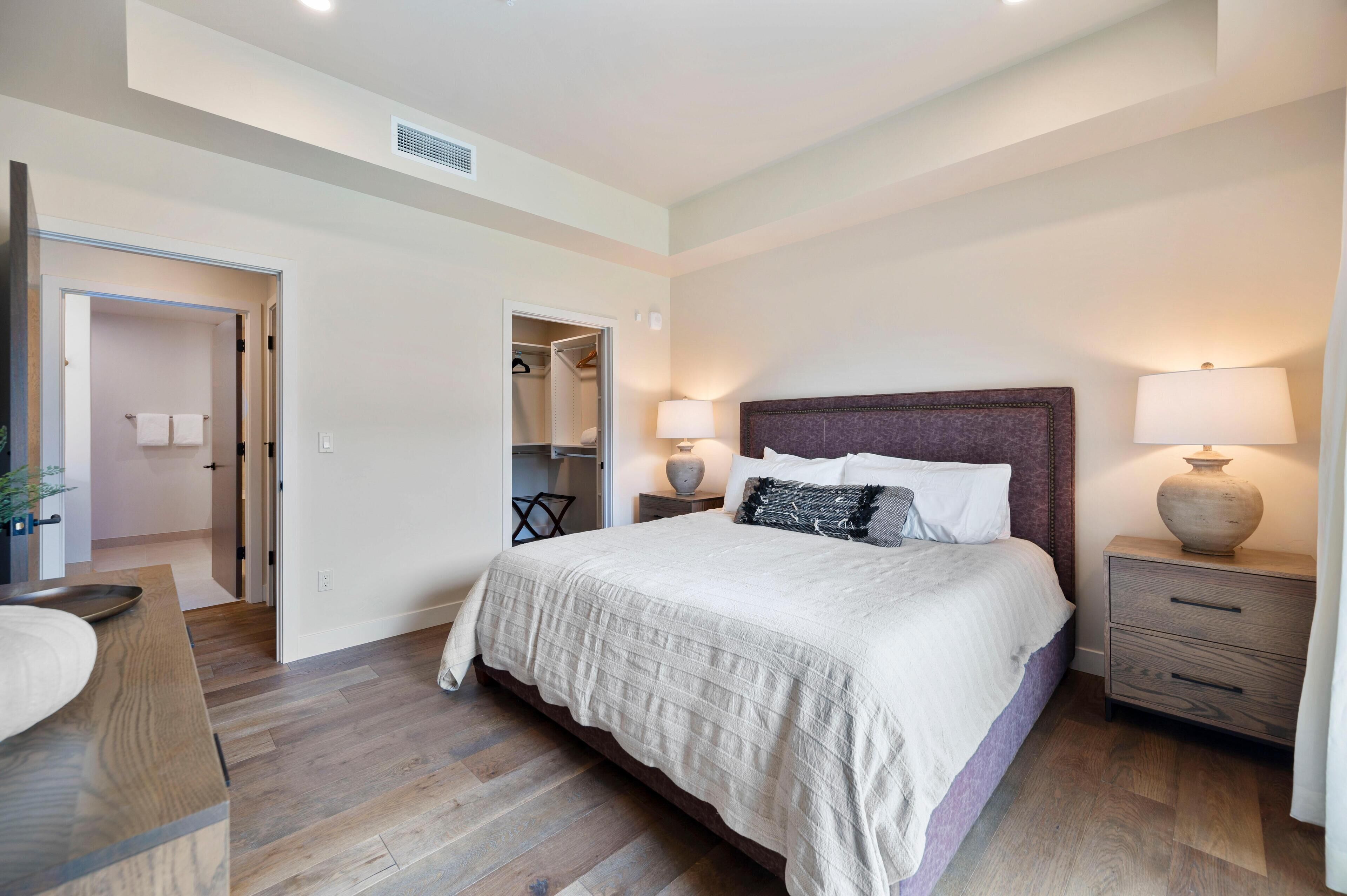 Un dormitorio con una cama grande, lámparas de noche, una mesita de noche de madera, un armario y un espejo.