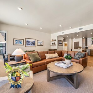 A modern living room with a brown leather sofa, a round coffee table, and a dining area with a lamp. - Slopeside | Exclusive Tamarack Perks (Tamarack)