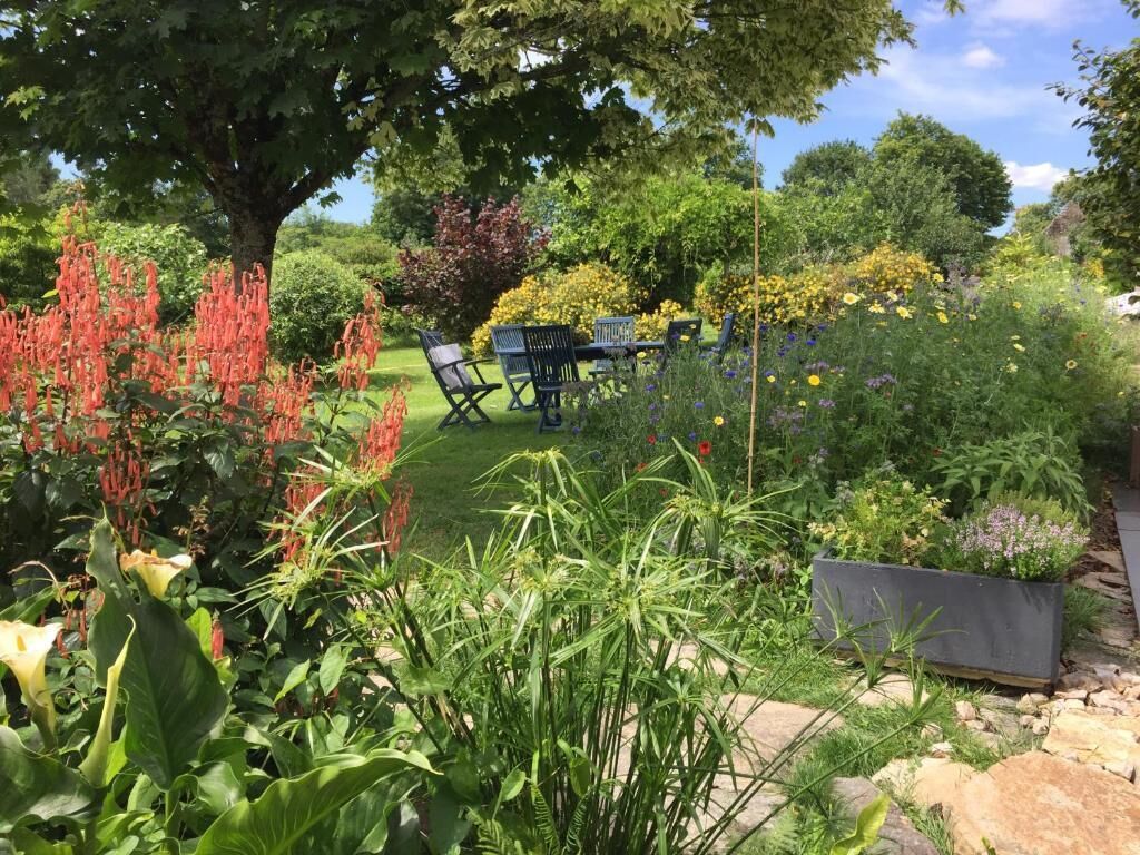 Ein Garten mit Tisch und Stühlen, umgeben von verschiedenen Pflanzen und Bäumen.