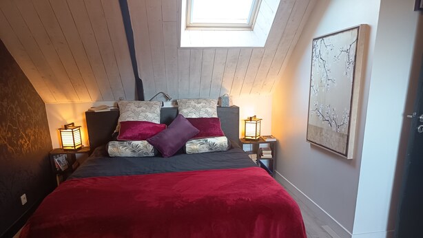 A bedroom with a skylight, a bed with patterned bedding, two bedside tables with lamps, and a wall-mounted artwork. - Les 3 Koïs (Riec-sur-Bélon)