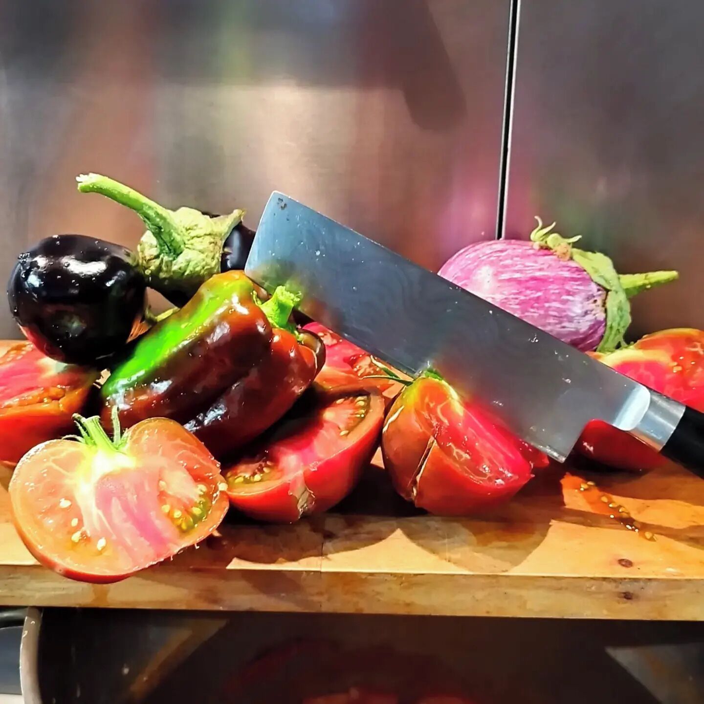 A variety of fresh vegetables on a cutting board with a large knife.